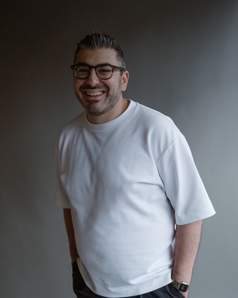 Serop Yildiz, laughing, in a white T-shirt against a dark wall